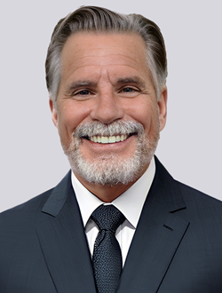 Smiling man in a suit with a beard, standing against a neutral background.