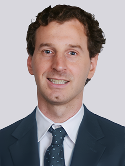 Portrait of a smiling man in a dark suit and polka dot tie against a light background.