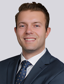 Smiling man in a blue suit and polka-dot tie, professional headshot with a neutral background.