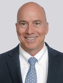 Smiling bald man in business attire with a blue tie, professional headshot against a light background.