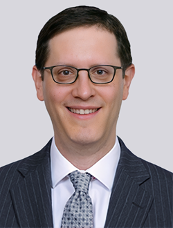 Man in suit and glasses smiling in professional headshot.
