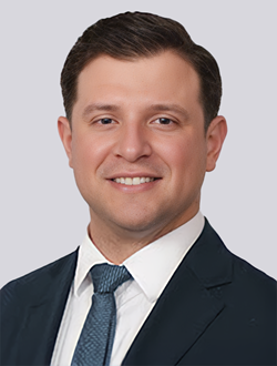 Professional man in suit and tie smiling against neutral background.