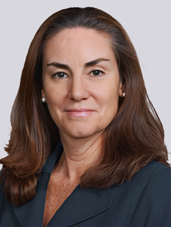 Professional woman in formal attire with dark hair, against a neutral background.
