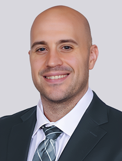 Smiling man in a suit and tie against a light gray background, business professional portrait.