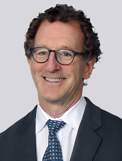 Smiling person wearing glasses and a suit with a patterned tie.