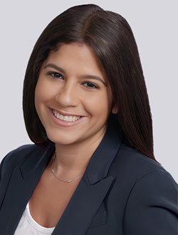 Smiling woman with long hair in a dark blazer, posing against a light background.
