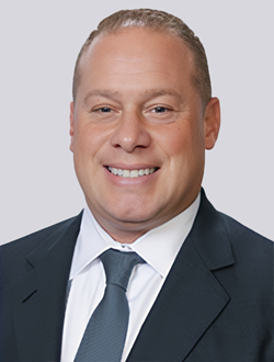 Smiling business professional in a suit and tie, with a light grey background. Ideal for corporate and professional contexts.