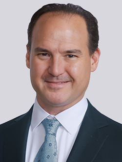 Business professional in suit and tie smiling, with a neutral background.