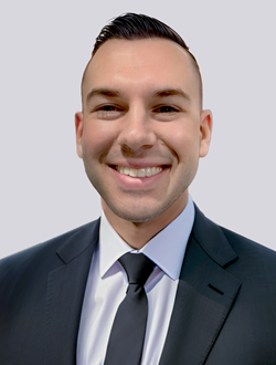 Smiling professional man in a dark suit and tie against a neutral background.