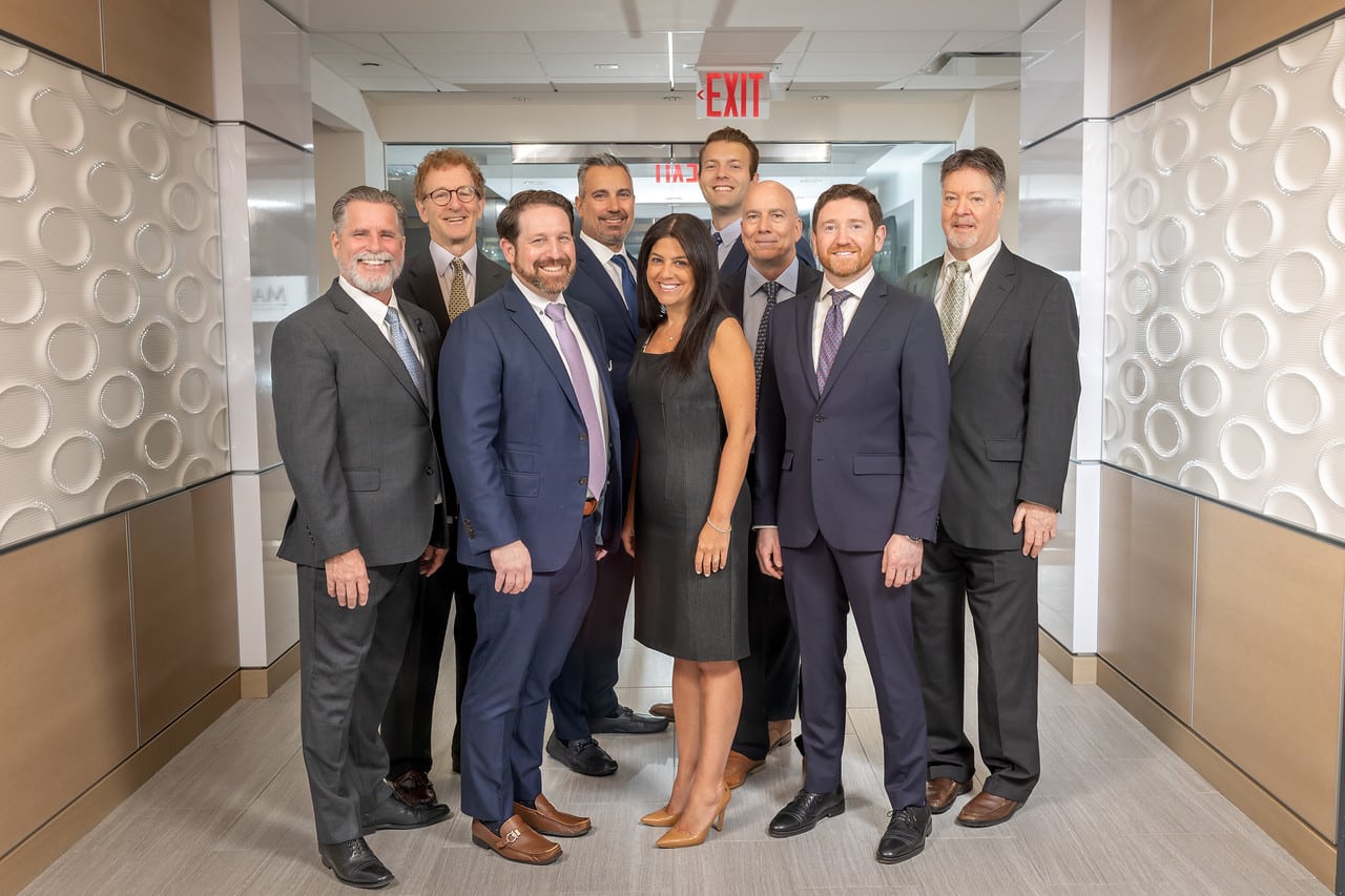 Professional team in business attire, standing and smiling in a modern office hallway.