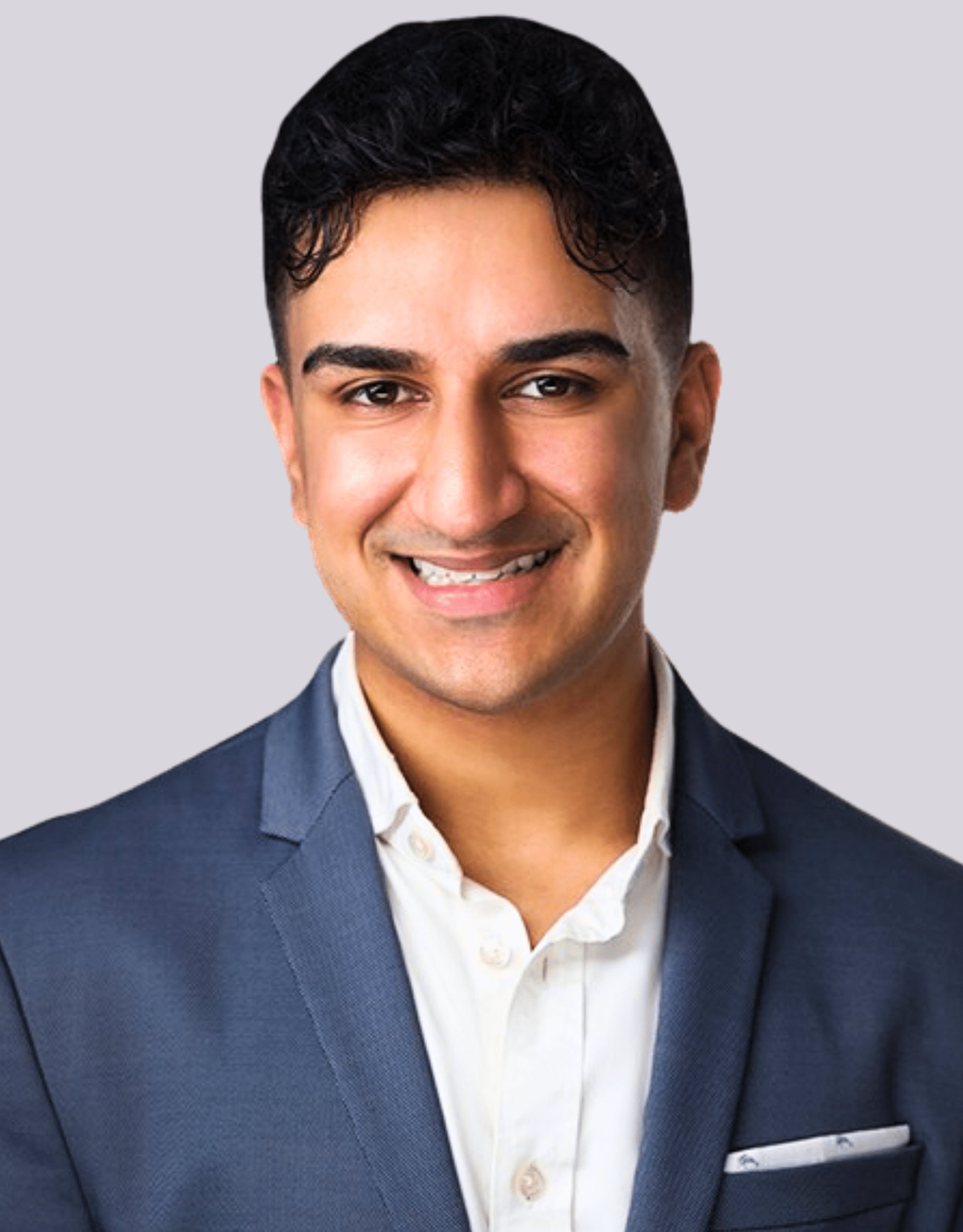 Professional headshot of a smiling person in a suit and white shirt, gray background.