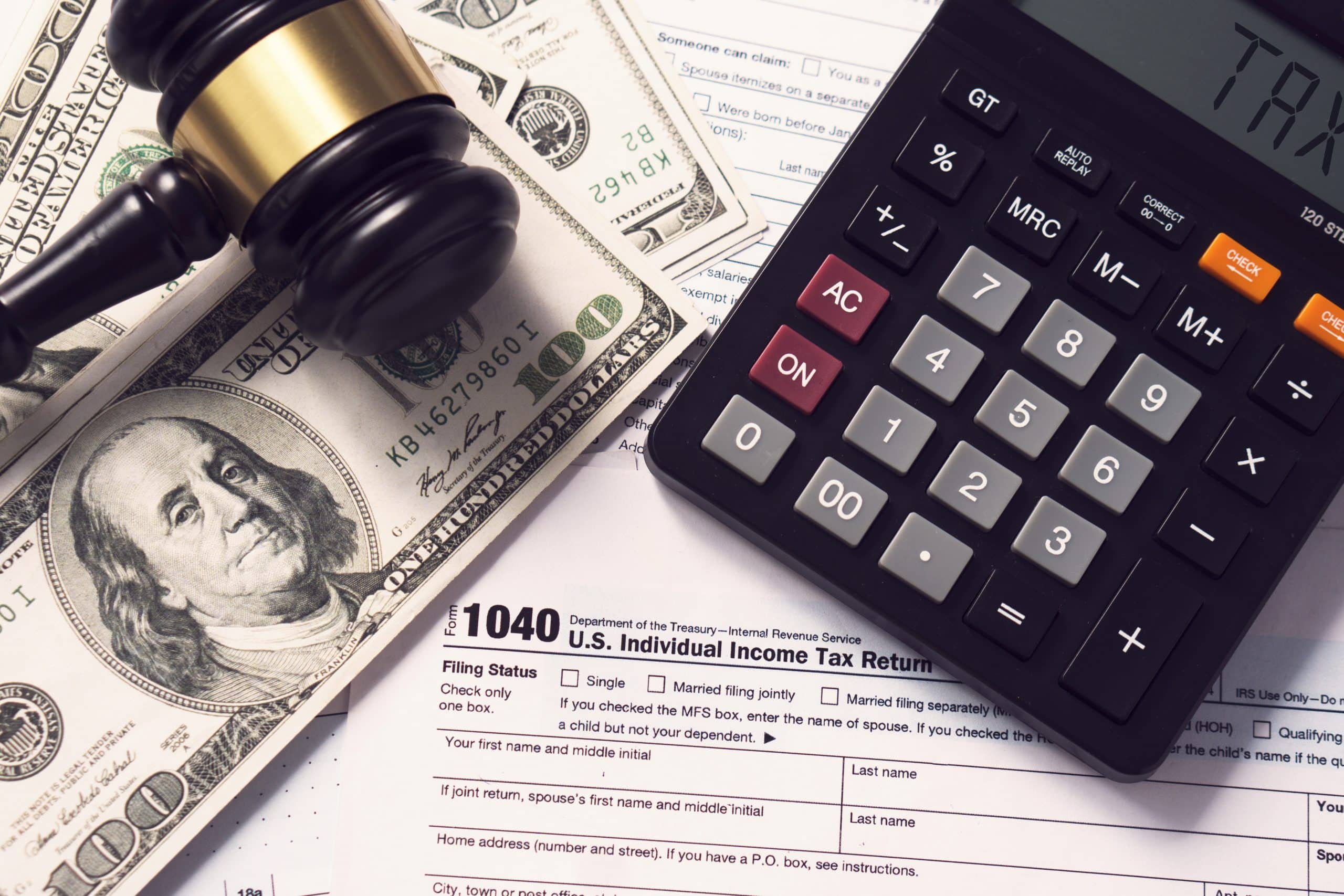 Calculator and gavel on U.S. tax form and dollar bills, symbolizing financial and legal aspects of tax filing.