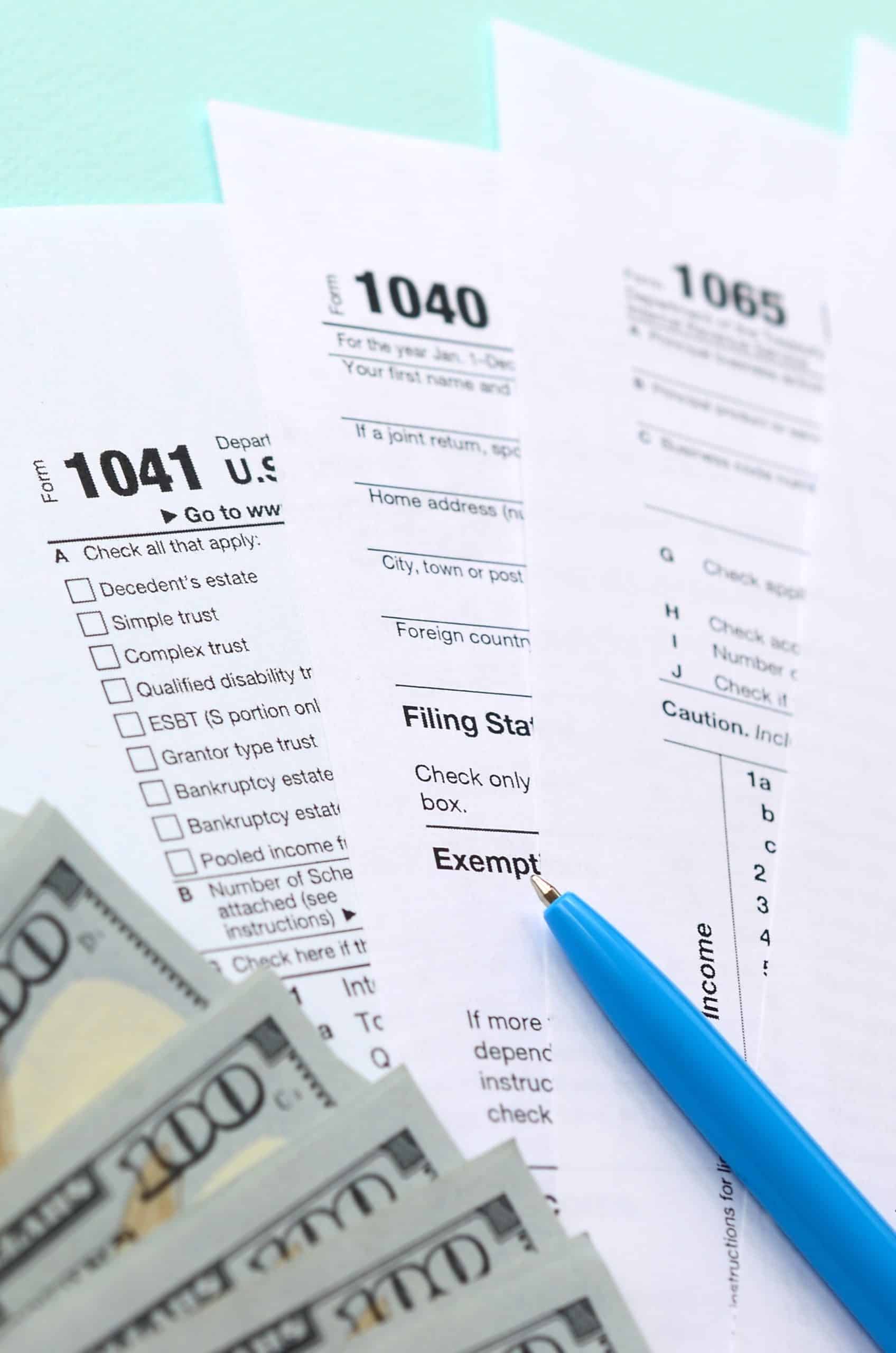 IRS tax forms 1040, 1041, and 1065 with blue pen and dollar bills, representing taxation and financial planning.